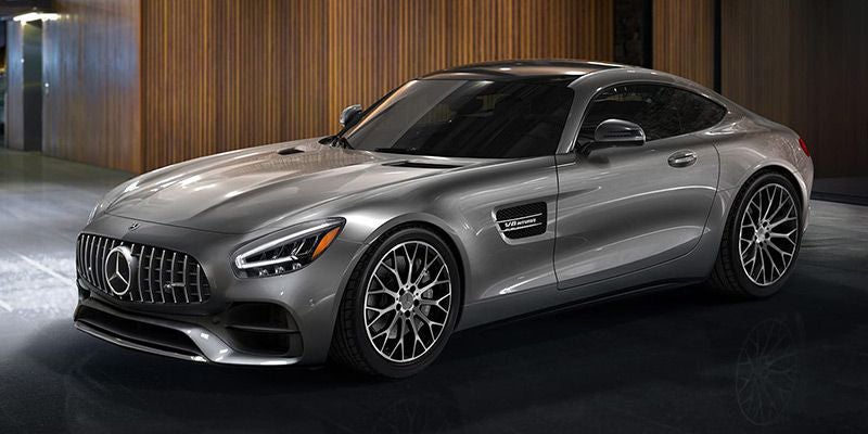 A sleek, light gray Mercedes-Benz AMG GT coupe parked indoors, angled to show its front and passenger side.