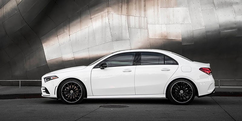 A white Mercedes-Benz A-Class sedan parked against a futuristic-looking silver corrugated metal wall
