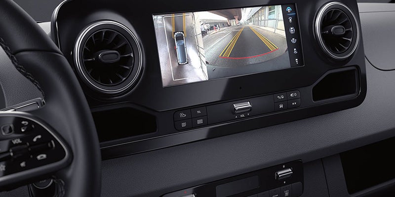 A bright, wide-angle backup camera view with parking guidelines and an overhead display of a vehicle, inside a car.