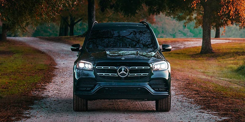 A black Mercedes-Benz GLE SUV parked on a dirt road, with trees and grass in the background