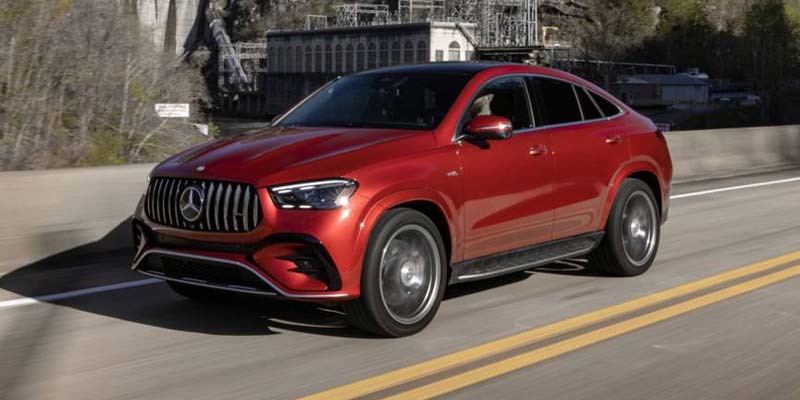 Red Mercedes-Benz coupe SUV driving on a paved road with a bridge and trees in the background