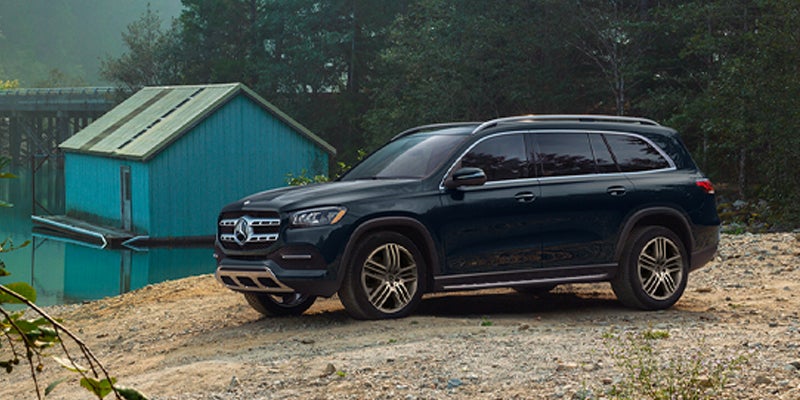 A black Mercedes-Benz GLS SUV parked on a dirt road, framed by autumn trees with orange and green leaves