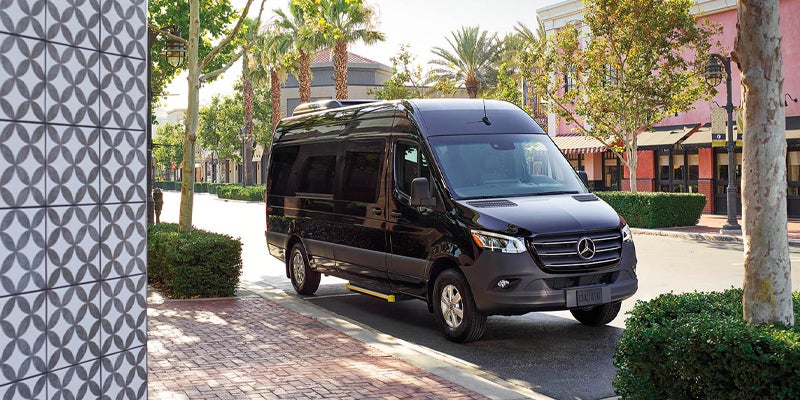 Black Mercedes-Benz Sprinter van parked along a tree-lined street in a commercial district