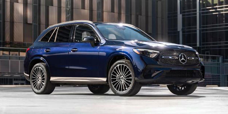 A shiny dark blue Mercedes-Benz SUV, angled slightly right, parked in front of a modern glass building.
