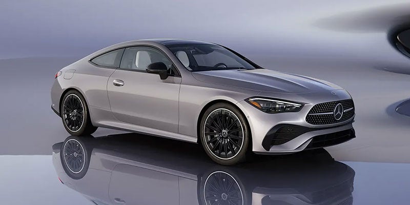 Silver luxury coupe on a reflective studio floor, shown from the front side angle