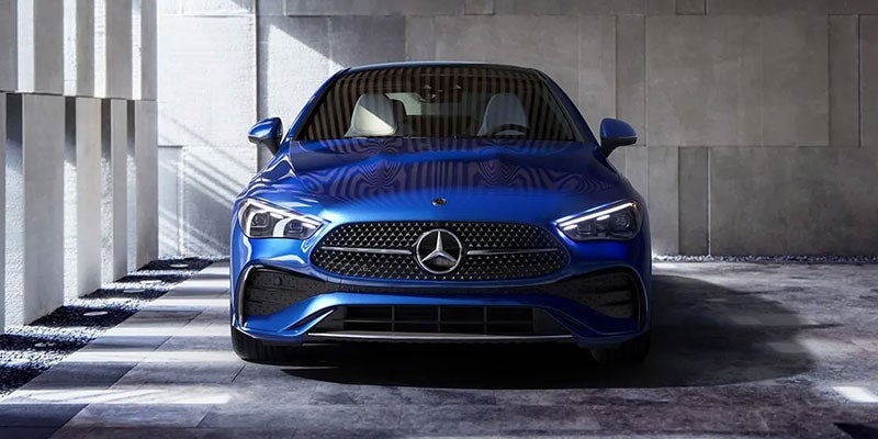 Front view of a shiny blue Mercedes-Benz sedan parked in an architectural garage with concrete walls.