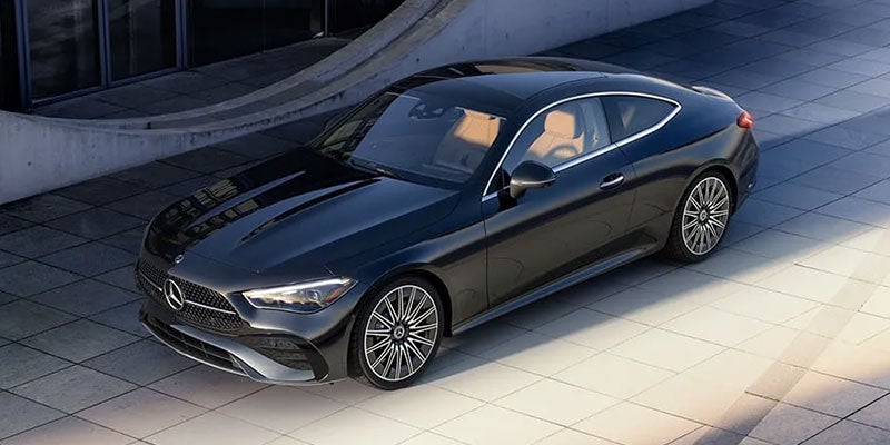 A dark grey Mercedes-Benz coupe with beige interior parked on light grey tiles, viewed from above, left side.