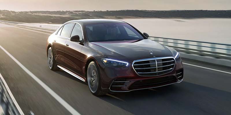 Mercedes-Benz S-Class luxury sedan traveling on a scenic roadway with waterfront views