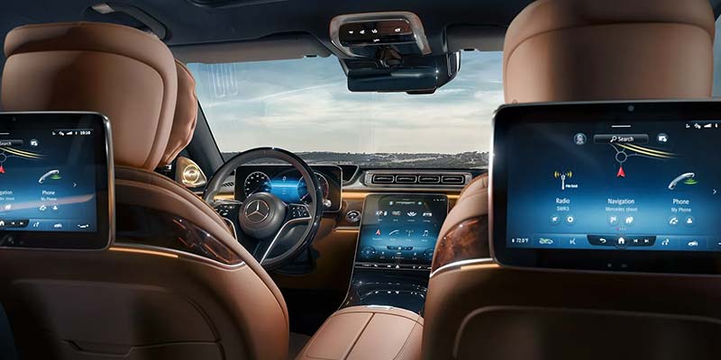 View of a luxury vehicle interior from the rear seats, showing tan leather upholstery, a digital driver display