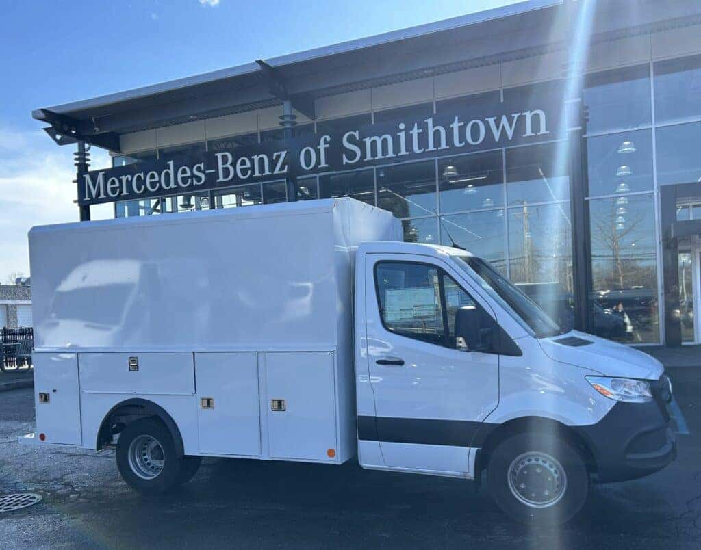 White Mercedes-Benz Sprinter work van with custom utility body parked in front of a Mercedes-Benz dealership.