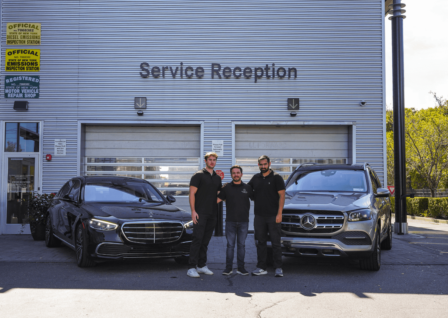 Three men standing by two Mercedes cars in front of a Service Reception building.