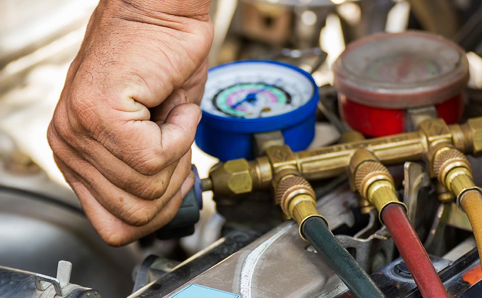 Technician connecting diagnostic gauges to a vehicle engine during automotive maintenance service