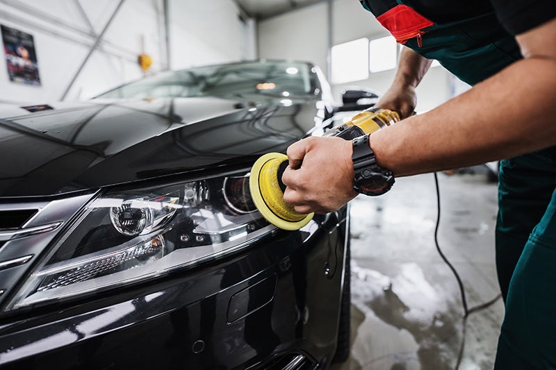 Automotive technician polishing the front headlight and body panel of a black vehicle