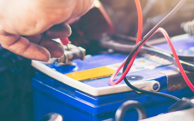 Technician testing a vehicle battery under the hood