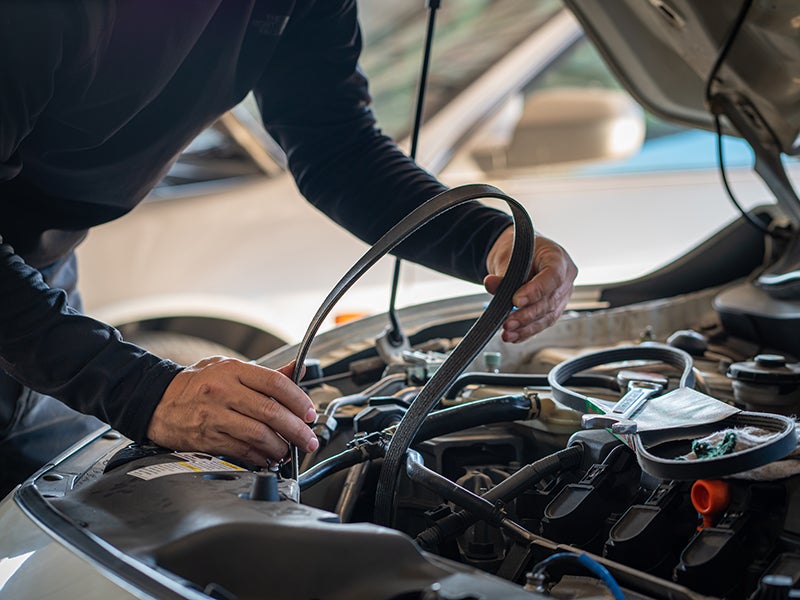 Automotive technician installing a serpentine belt under the hood of a vehicle