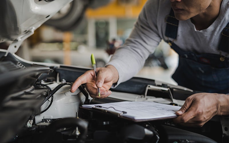 Technician completing a multi-point inspection checklist under the hood