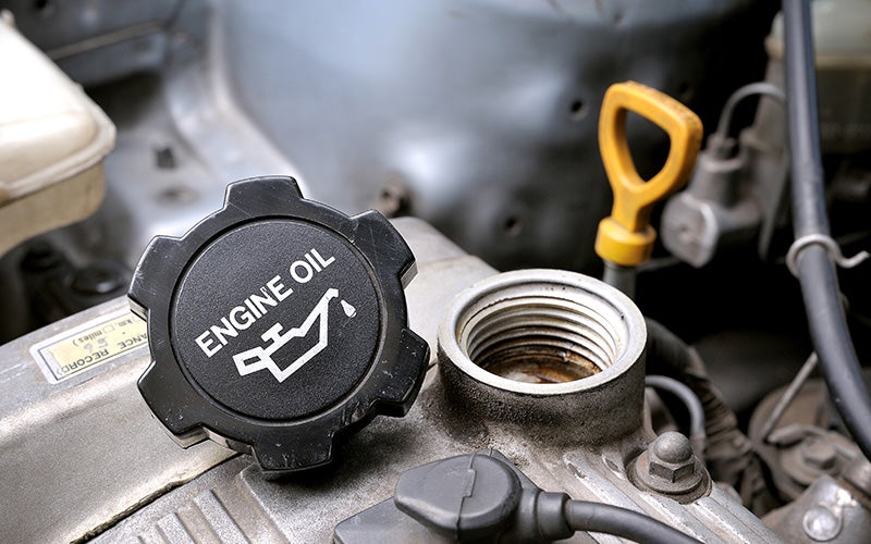 Close-up of a car engine with the Engine Oil cap removed, revealing the oil filler neck and a yellow dipstick handle