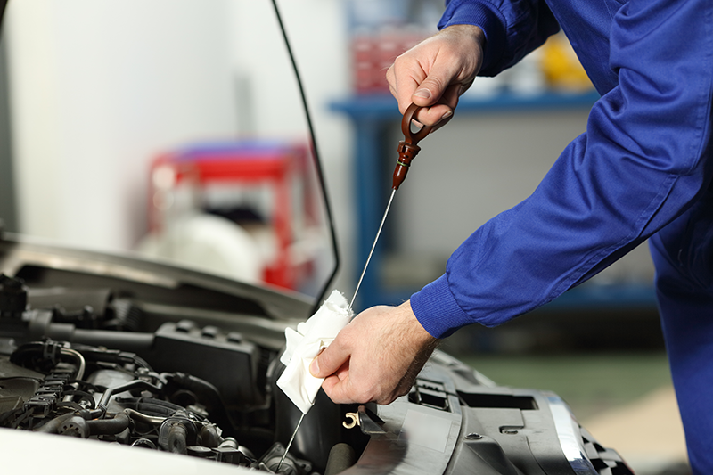 A mechanic in a blue uniform checks the oil level of a car with a dipstick and a white cloth