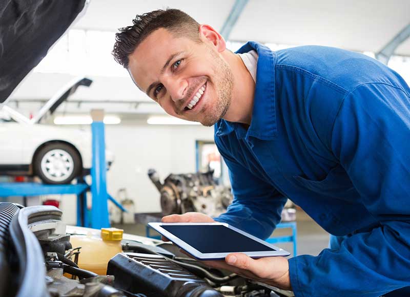 Automotive technician using a tablet while inspecting a vehicle engine in a service center