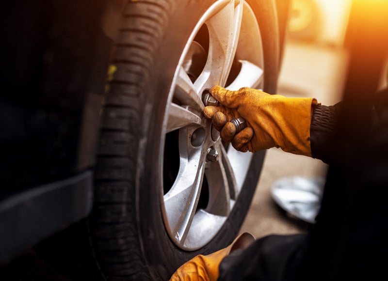 A person in orange gloves tightening lug nuts on a car wheel, replacing a tire.